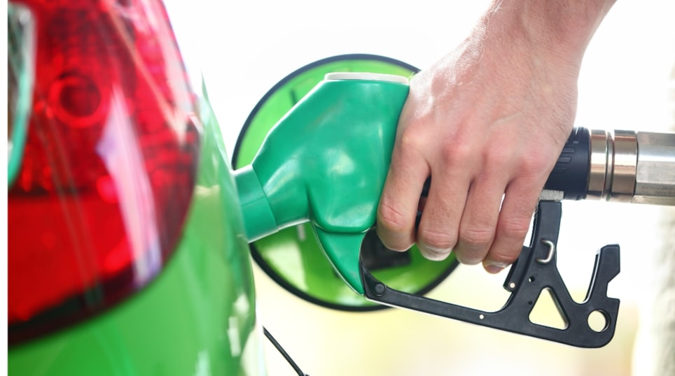 Hånd som holder drivstoffpumpe og fyller drivstoff på grønn bil