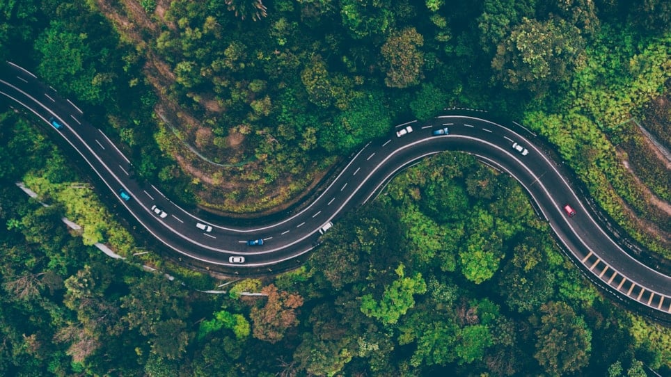 Dronefoto av vei med biler på med grønn skog rundt